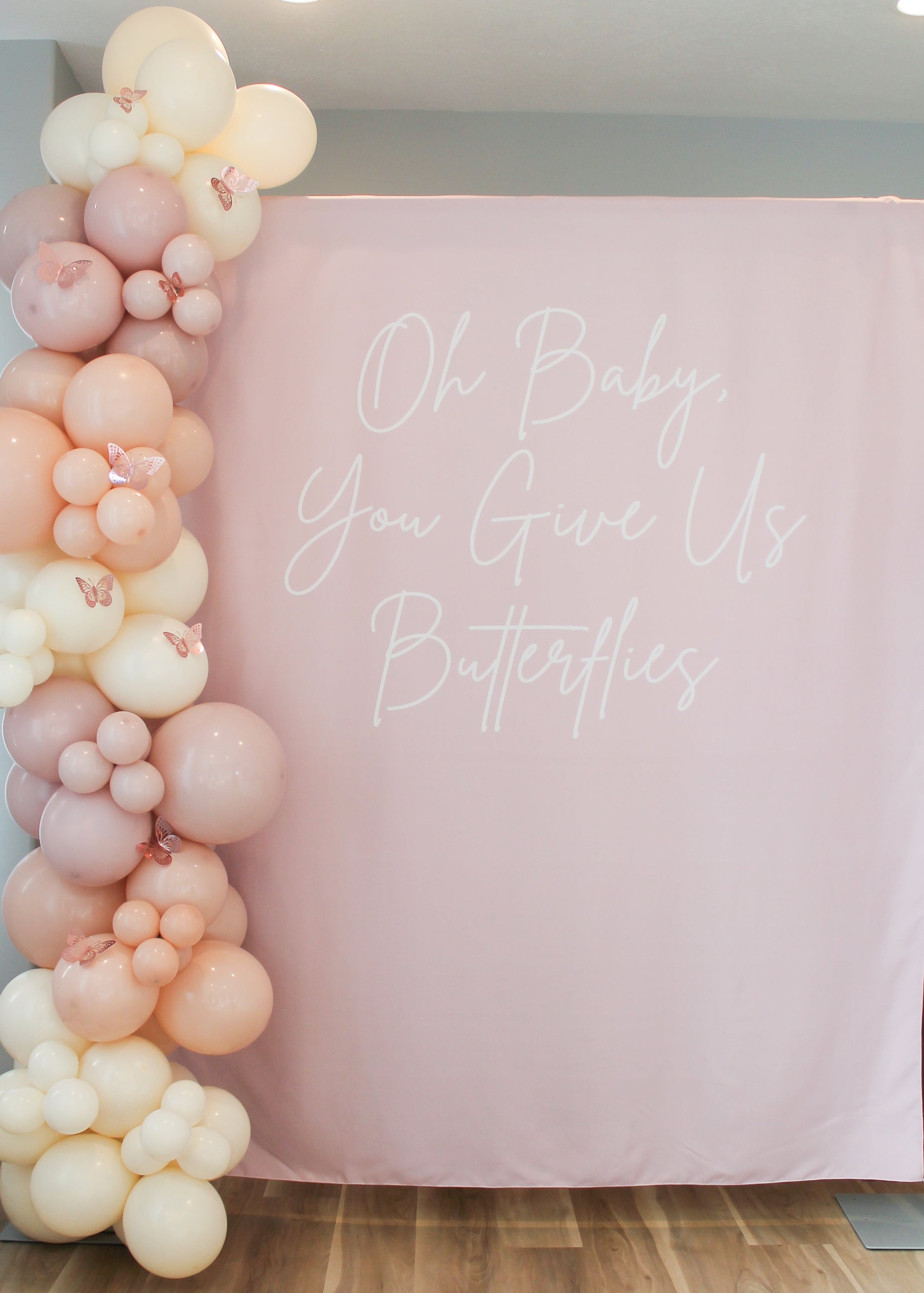 Balloon arch with pink and white balloons against a pink backdrop with text in a room.