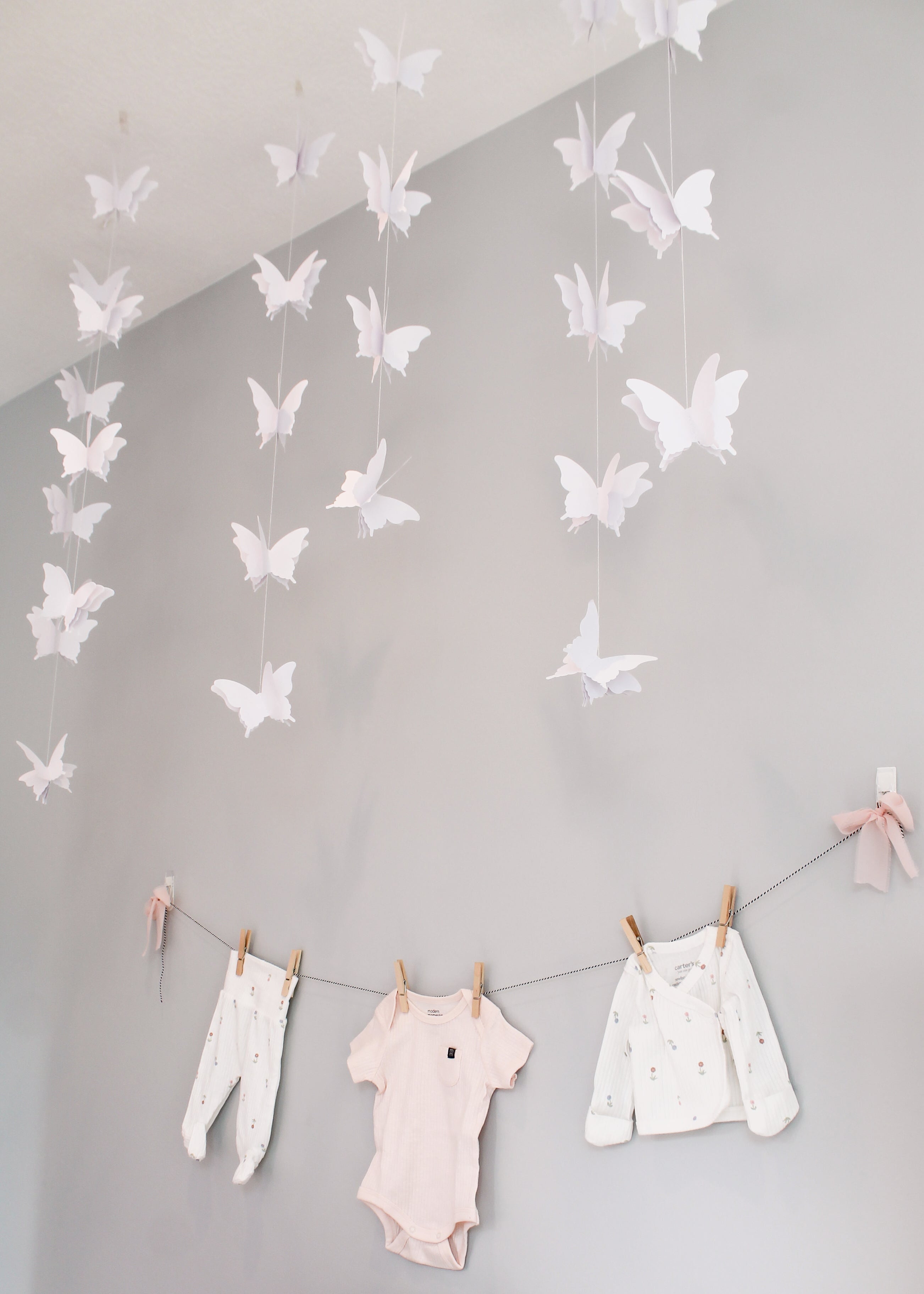 Butterfly garland hanging above baby clothes on a line against a gray wall.