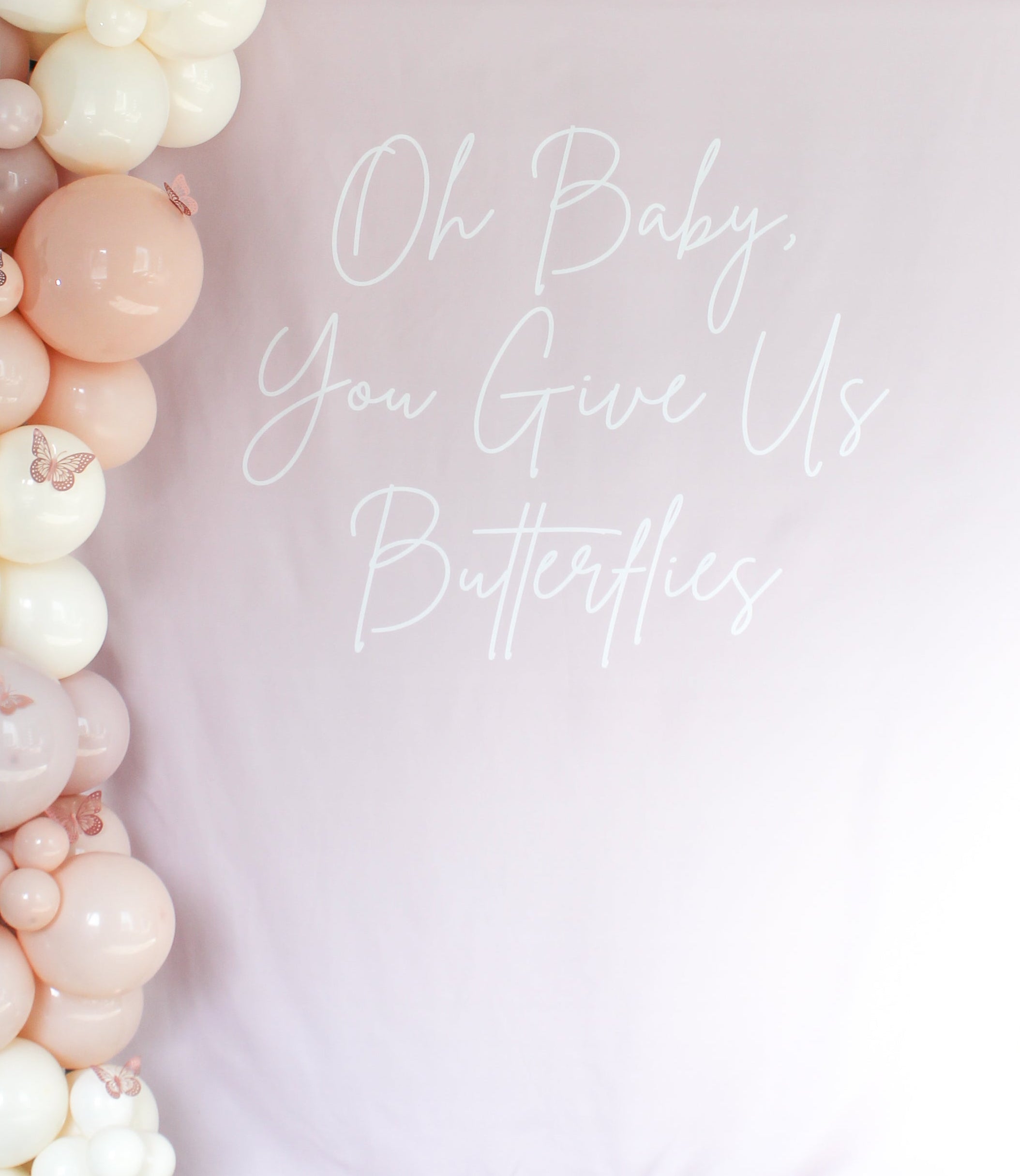 Balloon arch with text 'Oh Baby, You Give Us Butterflies' on a light pink background