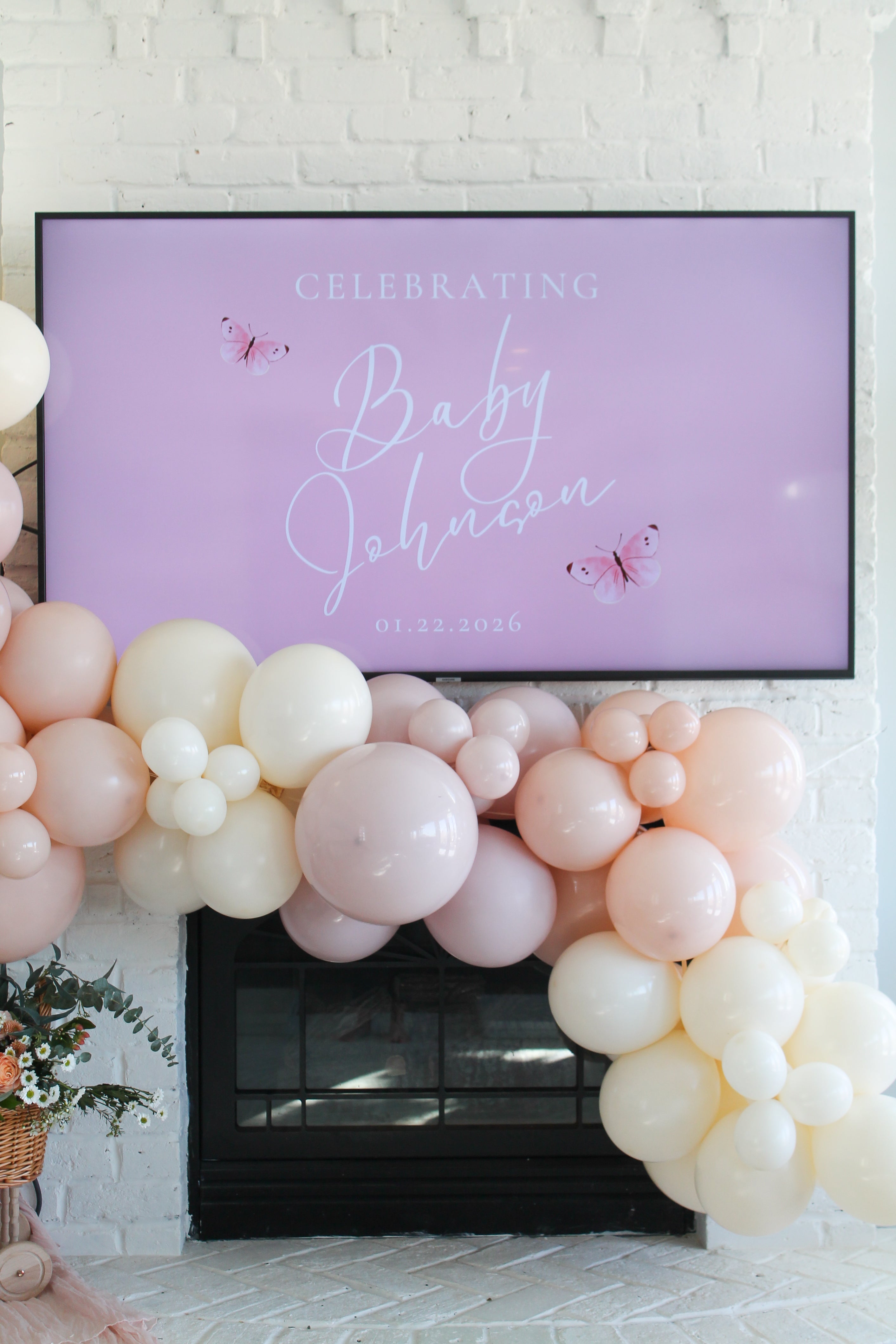Decorative balloon garland with a 'Celebrating Baby Johnson' sign on a white brick wall.