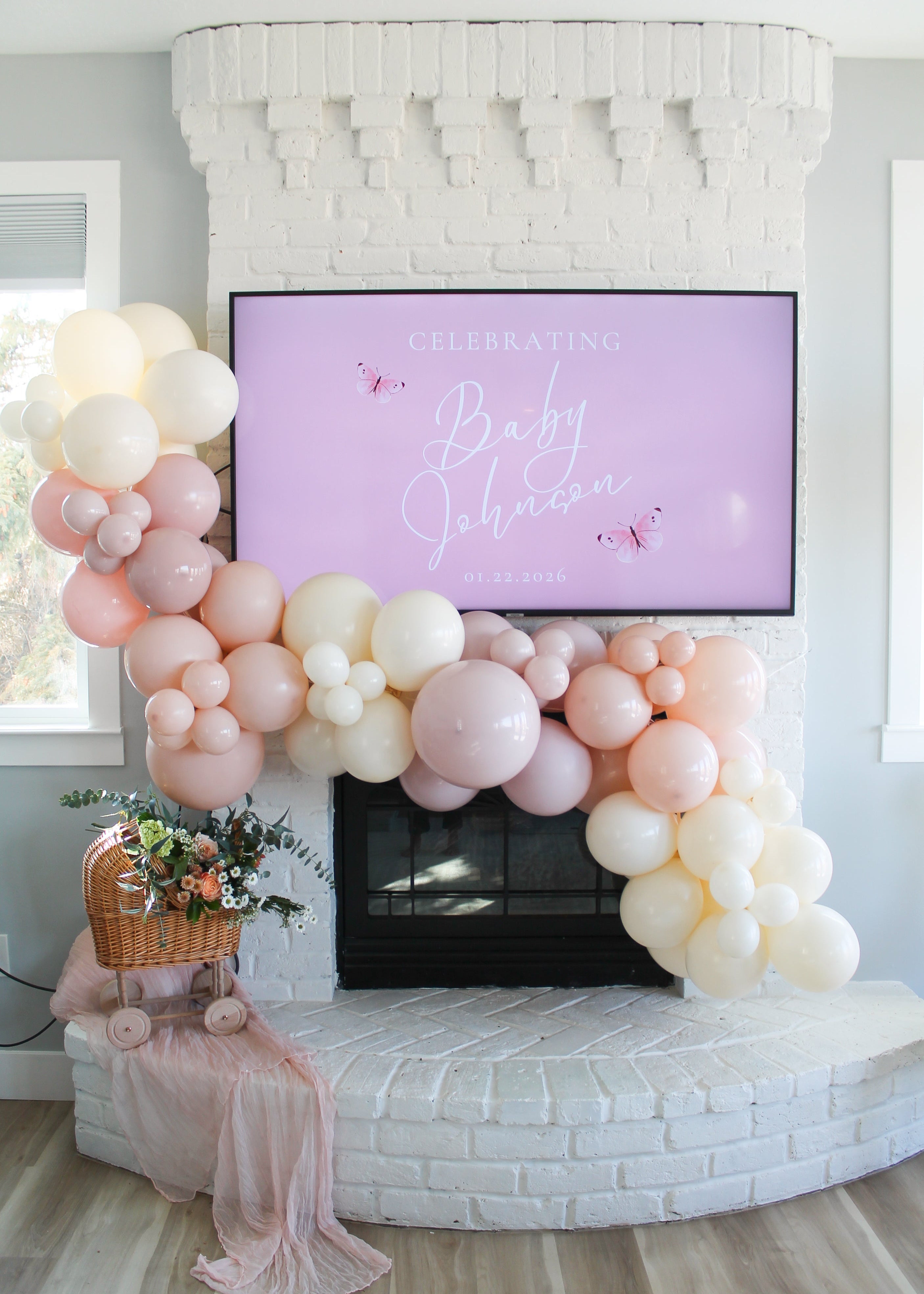 Balloon arch in front of a fireplace with a baby shower sign on a screen.