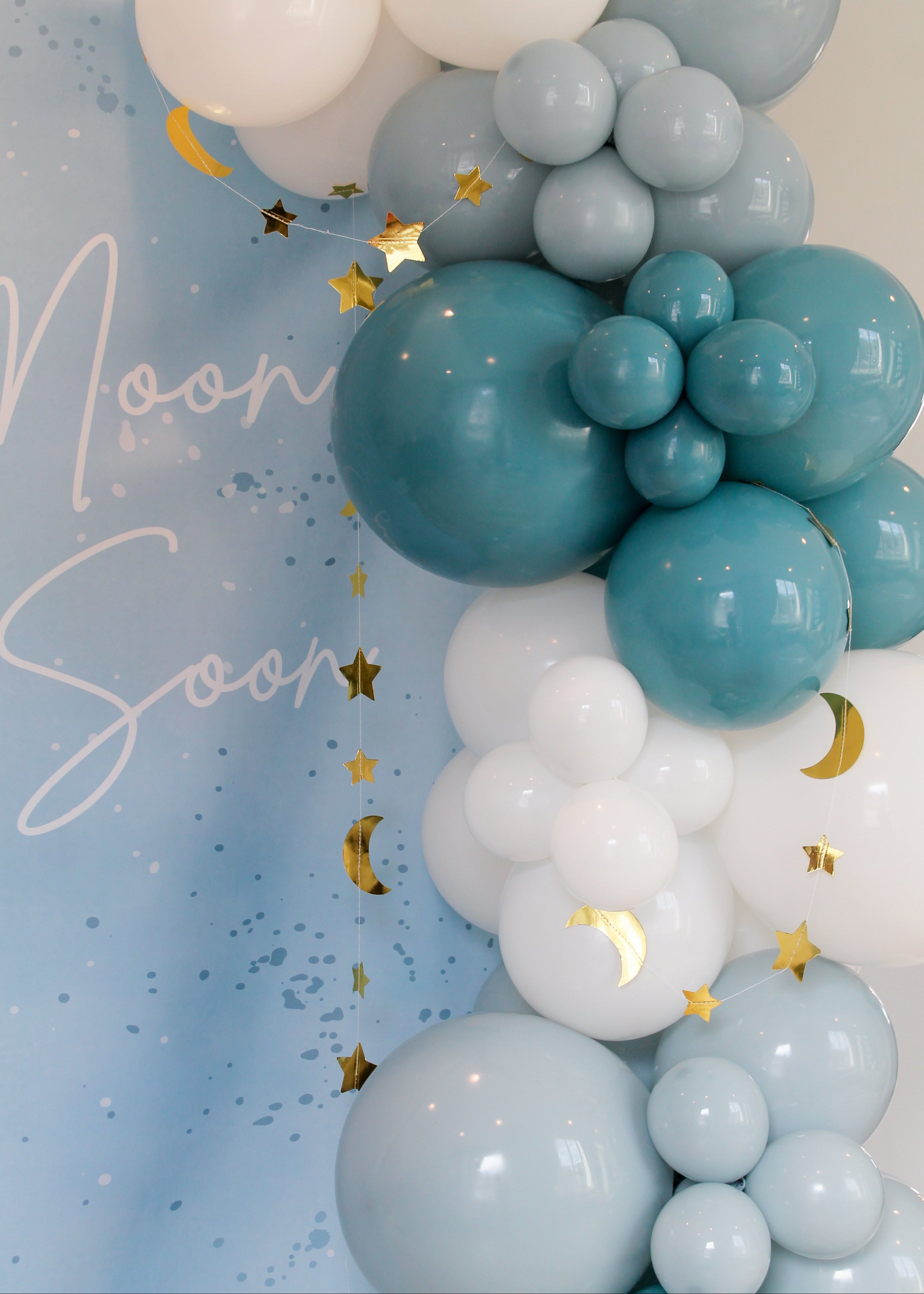 Balloon arch with teal, blue, and white balloons against a light blue background with decorative text and stars.