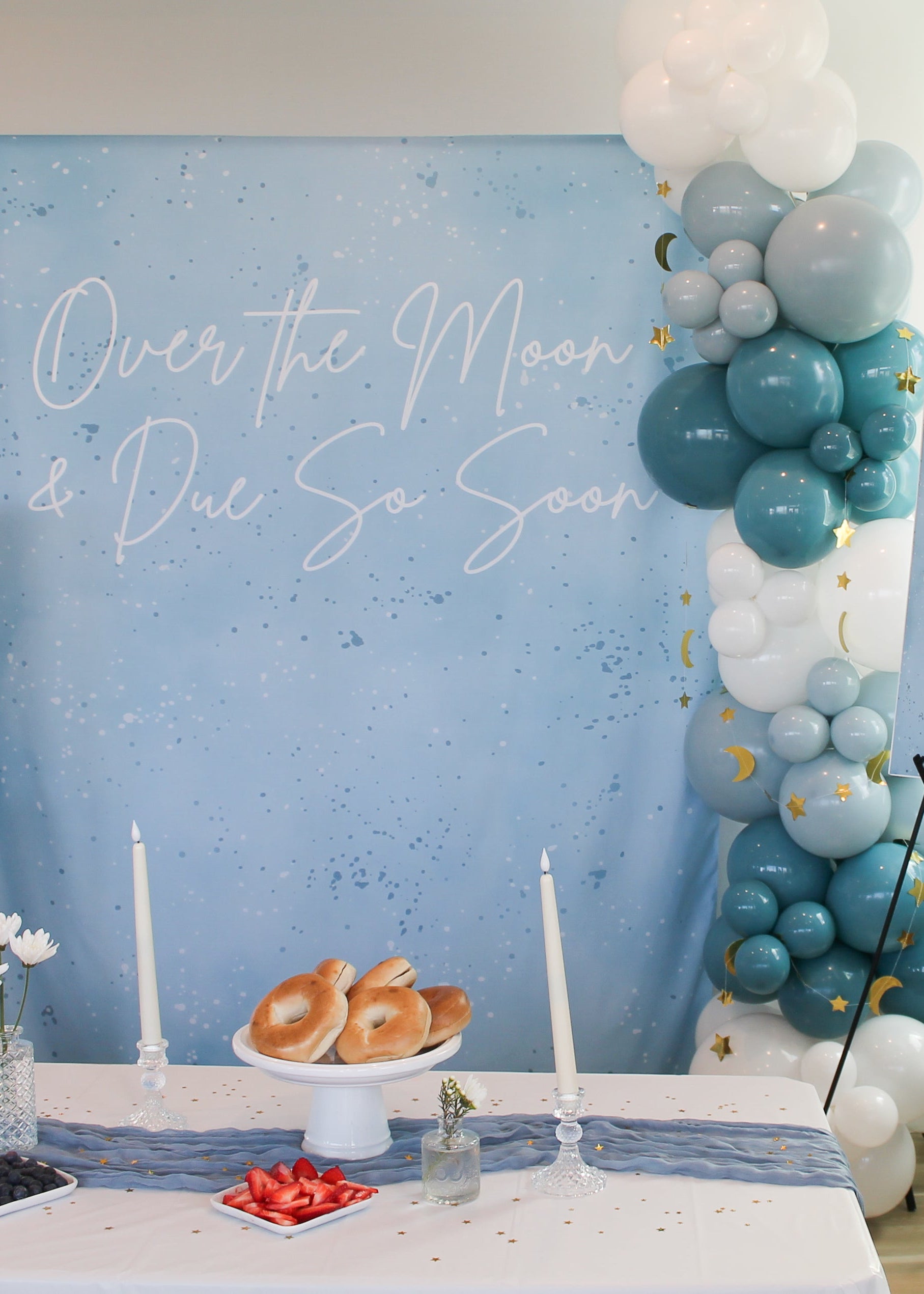 Baby shower setup with balloon arch, 'Over the Moon & Due So Soon' text, and food on a table.