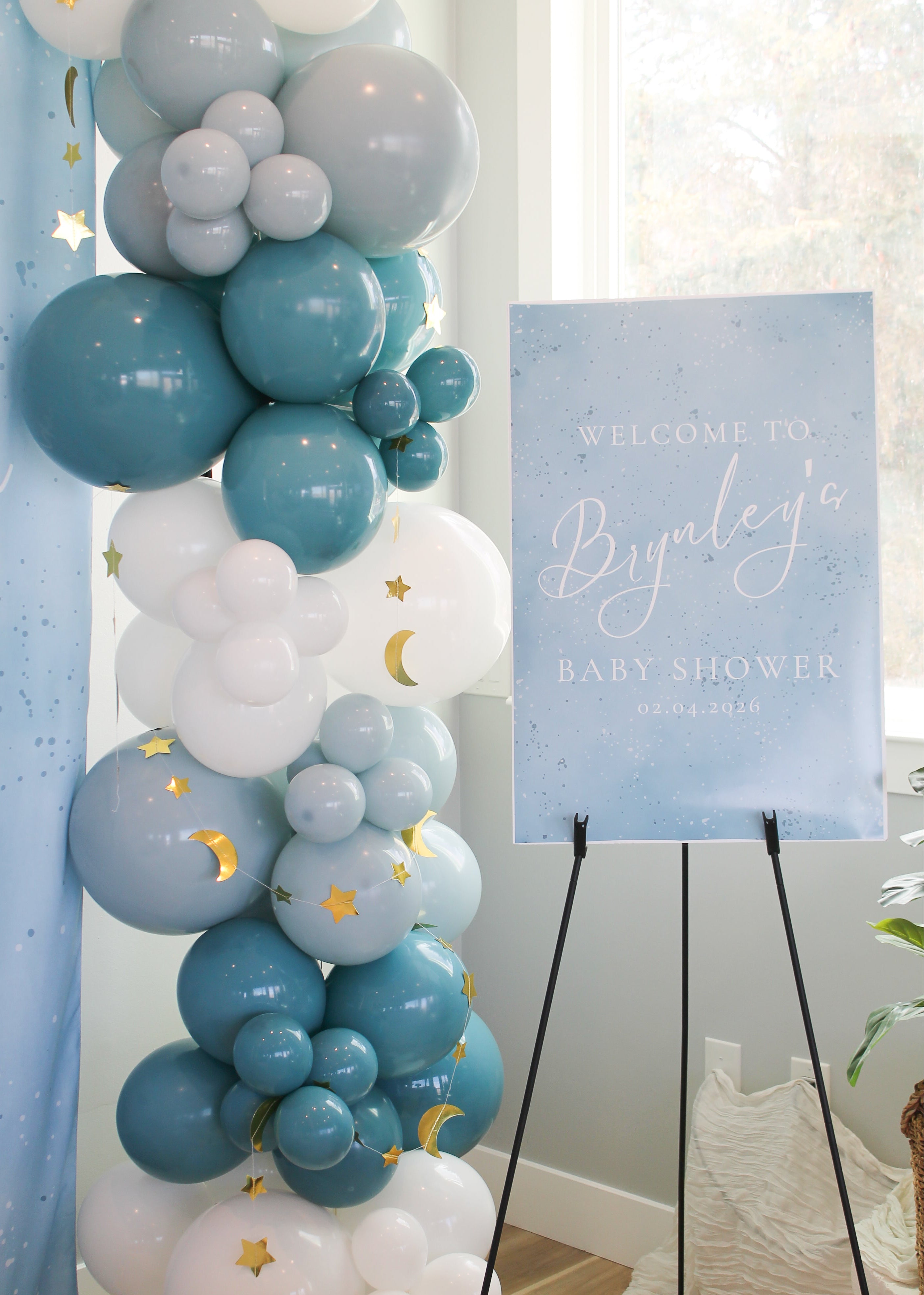 Balloon arch with blue, white, and gray balloons and a 'Welcome to Brynley's Baby Shower' sign.
