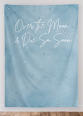 Blue textured wall tapestry with white text 'Over the Moon & Due So Soon' on a white wall.