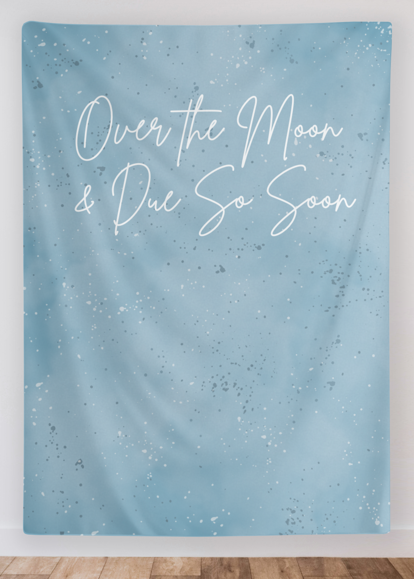 Blue textured wall tapestry with white text 'Over the Moon & Due So Soon' on a white wall.