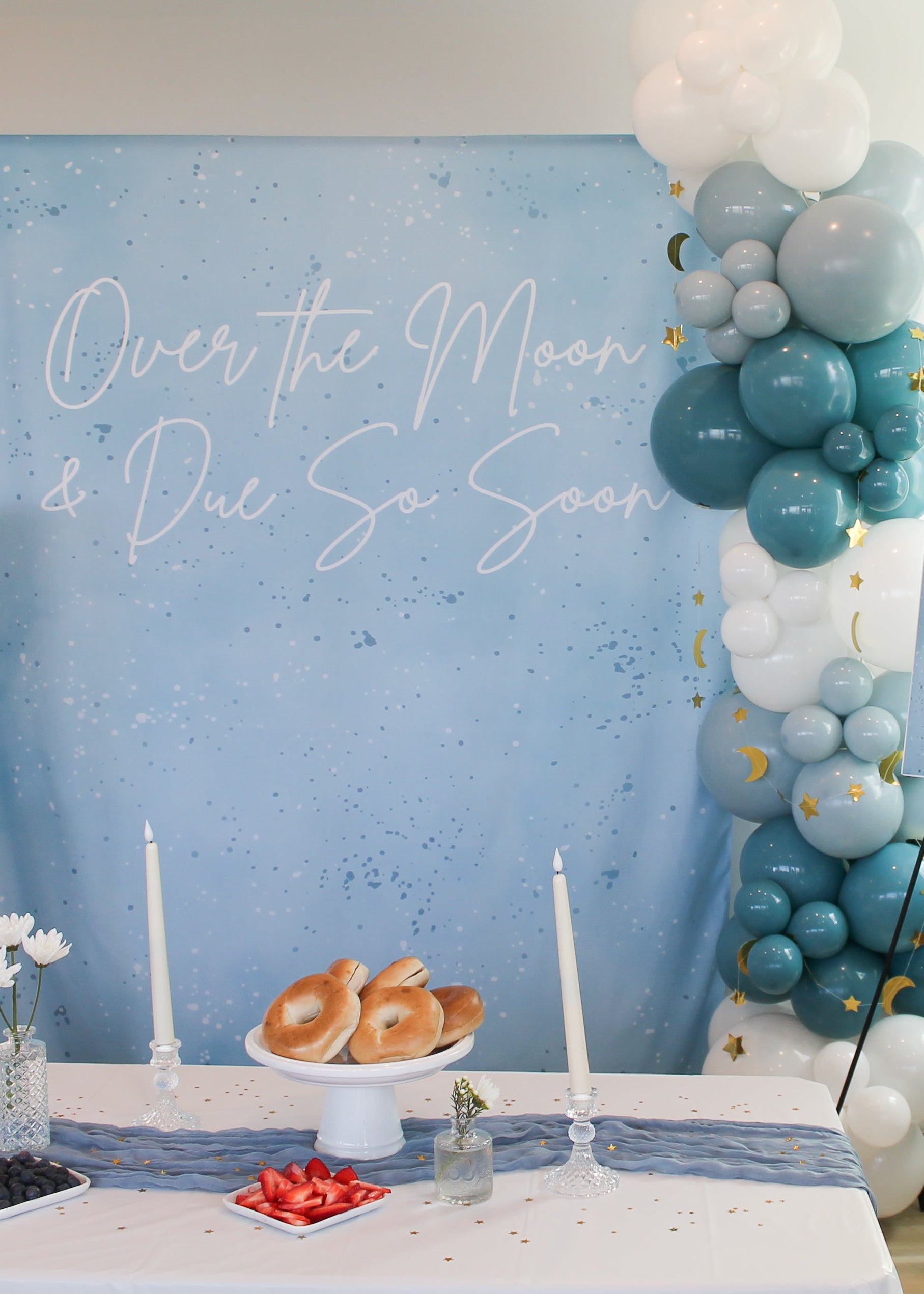 Baby shower setup with balloons, bagels, fruit, and 'Over the Moon & Due So Soon' backdrop.