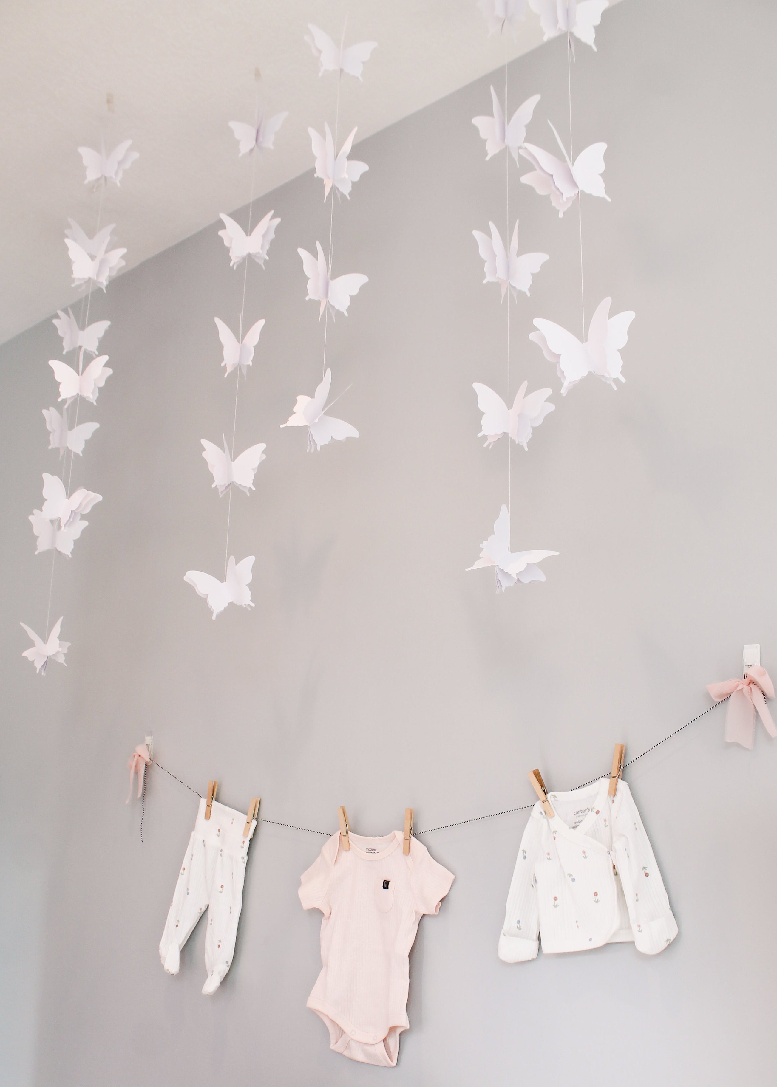 Butterfly decorations hanging from the ceiling with baby clothes on a line below.