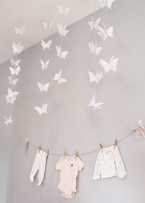 Butterfly decorations hanging from the ceiling with baby clothes on a line below.