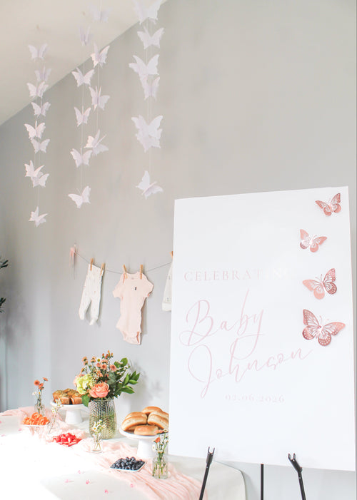 Decorative setup with butterfly decorations, a table with food, and a welcome sign with pink butterflies.