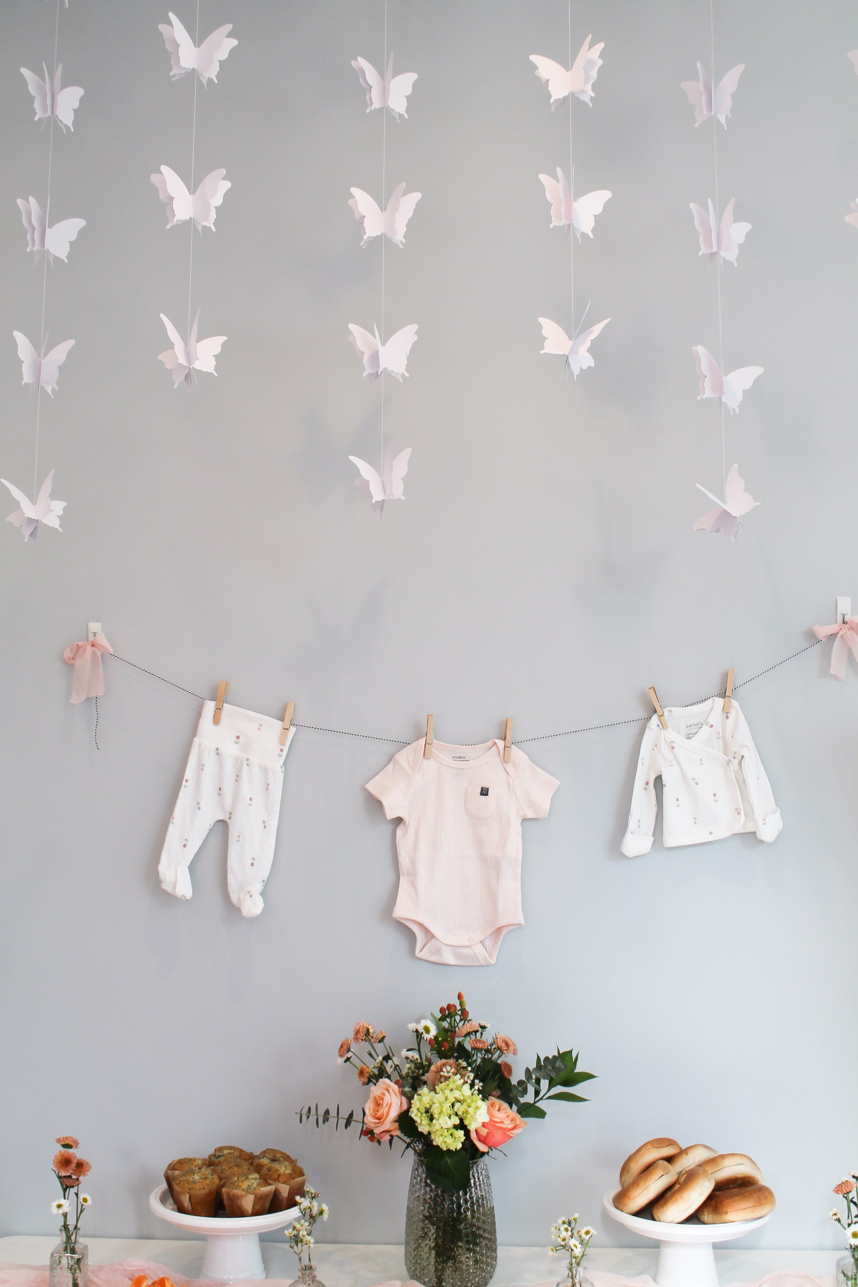 Baby clothes hanging on a line with butterfly decorations on a gray wall.